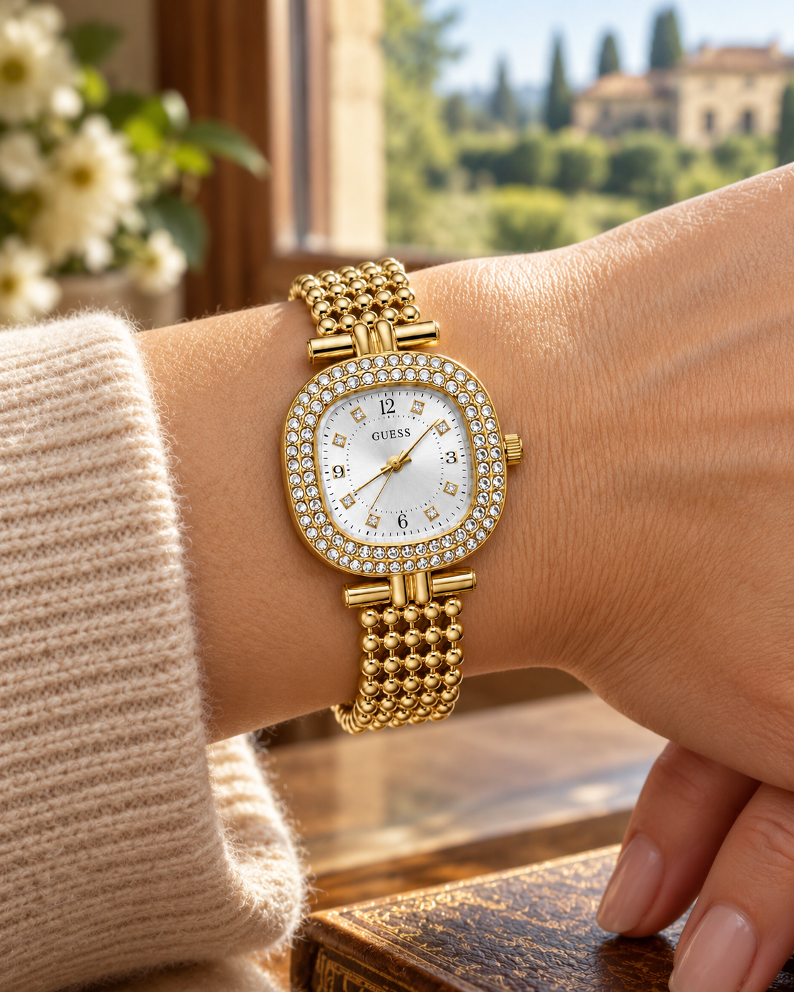 Guess women's watch on wrist Lebanon - gold-tone cushion case with double crystal bezel, silver dial (sunray finish) with crystal markers, beaded gold ball-chain bracelet